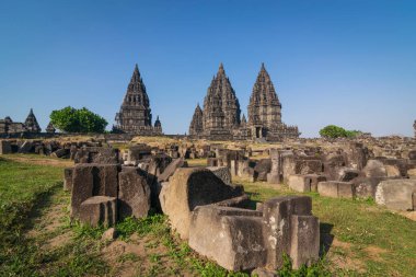 Bir UNESCO Dünya Mirası alanı olan Prambanan tapınağı manzarası. Endonezya Klaten 'de bulunan parlak mavi gökyüzünün altında muazzam, karmaşık oyulmuş taş yapılar görkemli bir şekilde yükselir..