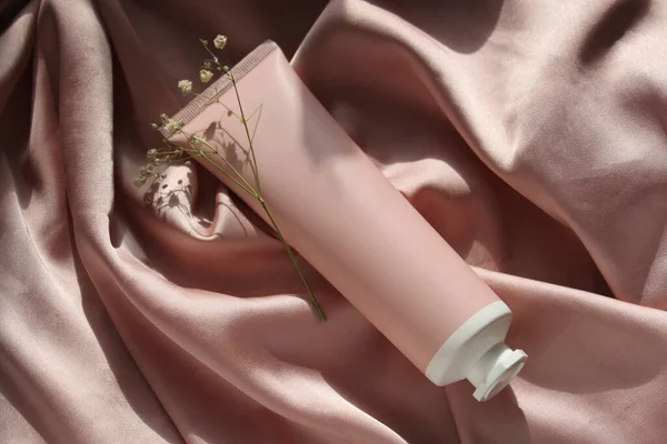 pink tube for cream on pink silk with flowers in the sunlight, moke up
