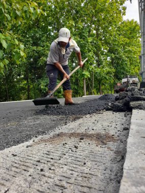 Asian male worker in a hat is scratching a pile of asphalt on the road in Indonesia