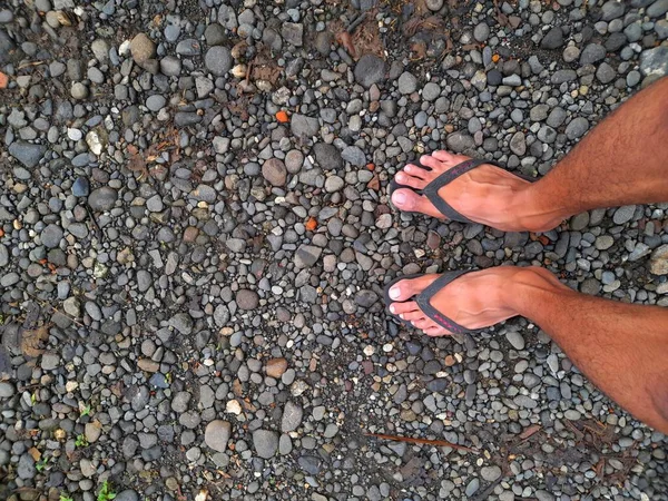 An asian man wearing sandals standing on small rocks