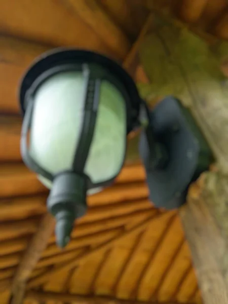 stock image Blurry photo of antique and minimalist garden lamp with white mirror and black stalk attached to a wooden pole against a wooden ceiling background