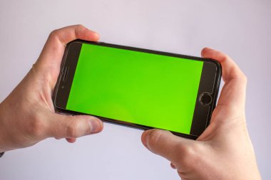 Çeşitli içerikler eklemek için elinde boş yeşil ekranlı bir cep telefonu var. Yeşil ekranlı akıllı telefon. Krom tuşlu telefon yakın plan.