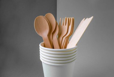 Arka planda bambu ahşap ve kağıttan yapılmış çevre dostu tek kullanımlık yemekler. Örtülü kaşıklar, çatallar, bıçaklar, kağıt bardaklı bambu tabaklar.