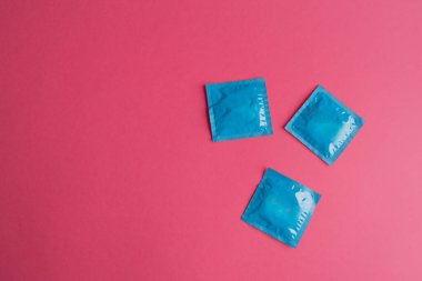 Pembe arka planda bir sürü mavi açılmamış prezervatif paketi var. Prezervatif kullanımı hamileliği veya cinsel yolla bulaşan hastalıkları azaltır. Güvenli seks ve üreme sağlığı kavramı.