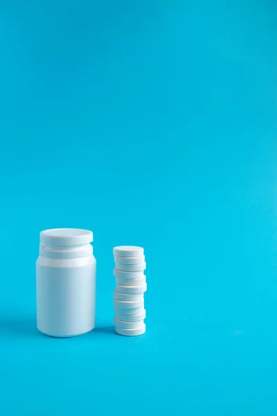 Plastic medical container and white tablets on a blue background viewed from the side. Medical and health concept. 3d rendering.