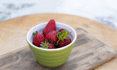 Dışarıdaki ahşap masada duran çilekli yeşil kasenin önü. Yaz kavramı.