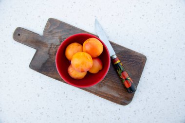 Tahta tahtanın üstünde turuncu erikli kase, kayısı ve mermer masada yatarken kesilmesi için bıçak. Yaz kavramı.