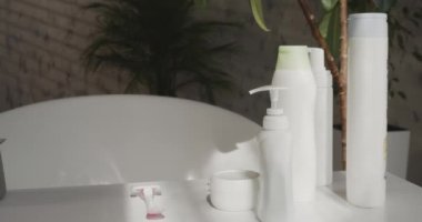 Tuvalette makyaj malzemesi olan kadın traşı, ağır çekimde. Kapalı sabun ve şampuan şişeleri, beyaz masa üzerinde yeşil bitkiler, kopyalama alanı ile. Sağlık, kaplıca, reklam kavramı..