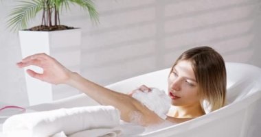 Evde köpük banyosu yapan çekici beyaz saçlı kadın. Yumuşak vücudu yıkayan hassas dişinin yukarıdan görünüşü, evde dinlenerek kaliteli boş zaman geçirmek. Vücut bakımı kavramı, spa.