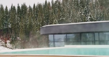 Gündüz vakti kayak merkezinde sıcak suyla birlikte açık yüzme havuzu. Termal havuz ve kayak kompleksinin panoramik manzarası, kışın çam ağacı ormanlarıyla çevrili, yavaş çekimde. Eğlence anlayışı, spa.