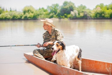Kırsalda balık tutarken güzel bir köpekle nehir boyunca yelken açan yorgun ve odaklanmış genç bir adam. Sıkıcı balıkçıların gündüz oltayı tutarken yüzen yüzeye bakışları. Balık tutma kavramı.