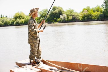 Kamuflajlı zayıf bir adam teknenin arkasında duruyor ve sabah sakin sularda balık yakalıyor. Erkek balıkçı oltayı tutarken sadık köpek kayığın dibinde dinleniyor. Birlikte dinlenme kavramı.