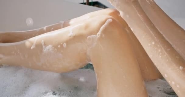 无法辨认的性感女人在泡泡浴中 在运动中 洗着光滑的腿 在阳光充足的浴室里 通过挤压浴缸海绵 让迷人的女性在腿上倒水 这让人眼前一亮 沐浴过程概念 — 图库视频影像