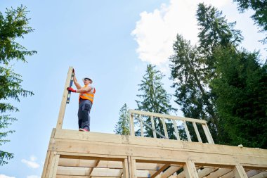 Uzman müteahhitin dik duruşu, tutuşu, tutuşu, ölçümü, tahta yaldızı. Erkek işçi, mühendis binası, inşaat, kask takmak. İnşa kavramı,