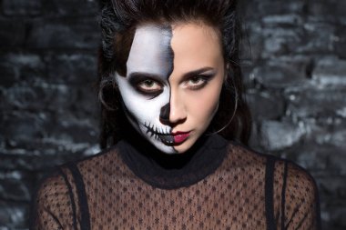 Kafatası makyajcısı kız. Karanlık stüdyoda kameraya bakıyor. Güzel, ciddi bir kadının portresi. Kafatası gibi vücudu ve esrarengiz bir görünüşü var. Cadılar Bayramı konsepti.