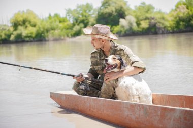 Uçan balıkçı, eski bir teknede nehirde yürürken benekli köpeği okşuyor. Kamuflaj kıyafetli dalgın bir erkek balık tutarken sevimli bir evcil hayvana sarılıyor, bulanık bir geçmişi var. Erkek hobisi kavramı.