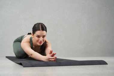 Çekici orta yaşlı bir kadın yoga minderinin üzerinde bacak bacak bacak üstüne atıyor. Yoga dersi sırasında eğreltiotu rengi etek giyen, gülümseyen, koyu renk saçlı bayanın yakın görüntüsü. Yoga konsepti.