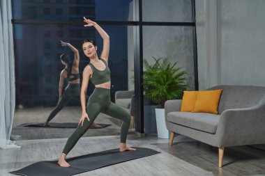 Güzel esmer, gece rahat bir odada antrenmandan önce rahat bir giysi giyiyor. Cama doğru zarif bir şekilde uzanan sportif bayanın ön görüntüsü. Spor anlayışı, yaşam tarzı.