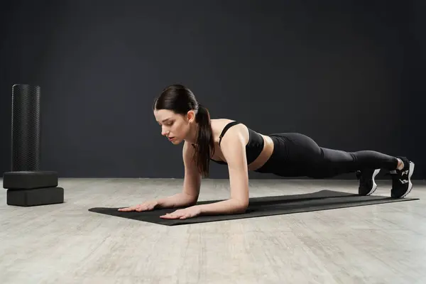 Brunette sportswoman standing in plank position on yoga mat, while training hard in gym. Side view of determined caucasian girl in activewear keeping body in tense, doing plank. Concept of sport.