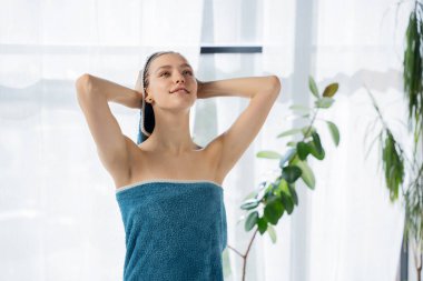 Hayalperest, genç bir kadın banyodan çıktıktan sonra turkuaz havluya saç sarıyor. Havlu giymiş mutlu bir kızın portresi banyoda ıslak kafasını geniş pencereye yaslıyor. Saç bakımı kavramı, güzellik.