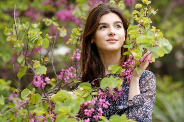 Güzel, esmer bir kadının park yerinde durup pembe çiçekleri tutarak gülümsediğini görmek. İlkbahar kavramı.