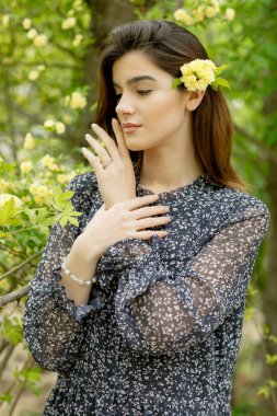 Çiçek açan bahçede duran zarif kızın yan görünüşü, aşağı bakan, elini kaldıran, yüze dokunan. İlkbahar kavramı.