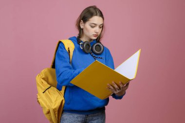 Önde duran esmer kız öğrenci, elinde klasör, okuyor. Mavi khudi ve kot pantolon giyen, kulaklık takan, aşağı bakan güzel bir bayan. Modern yaşam tarzı kavramı.