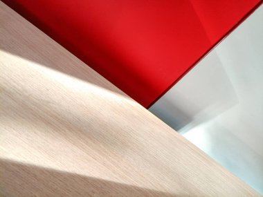 Minimalist tarzda soyut bulanık arkaplan, ahşap bir masa üstüyle kırmızı ve beyaz bir zemin örtüşüyor. Güneş ışığı yüzeyde güzel bir şekilde parlıyor..