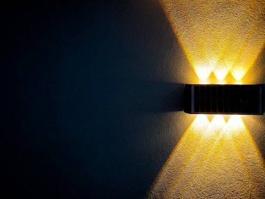 Duvardaki lambanın minimalist tarzı fotoğrafı. Güzel sarı ışık bir grafik çizgisi deseninde parlar. Resme benzersiz bir bakış açısı verir. Metin için yer vardır..