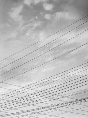 Yüksek voltajlı elektrik hatlarının minimalist siyah beyaz fotoğrafı gökyüzü arka planıyla kesişiyor ve eşsiz ve güzel bir görüntü oluşturuyor..