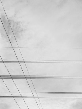 Yüksek voltajlı elektrik hatlarının minimalist siyah beyaz fotoğrafı gökyüzü arka planıyla kesişiyor ve eşsiz ve güzel bir görüntü oluşturuyor..