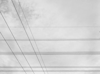 Yüksek voltajlı elektrik hatlarının minimalist siyah beyaz fotoğrafı gökyüzü arka planıyla kesişiyor ve eşsiz ve güzel bir görüntü oluşturuyor..