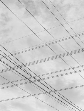 Yüksek voltajlı elektrik hatlarının minimalist siyah beyaz fotoğrafı gökyüzü arka planıyla kesişiyor ve eşsiz ve güzel bir görüntü oluşturuyor..