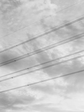 Yüksek voltajlı elektrik hatlarının minimalist siyah beyaz fotoğrafı gökyüzü arka planıyla kesişiyor ve eşsiz ve güzel bir görüntü oluşturuyor..