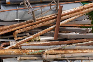 Eski paslı metal borular bir çöp sahasında yatıyor. İnşaat atıklarının yol açtığı çevre kirliliği. Paslı su boruları.