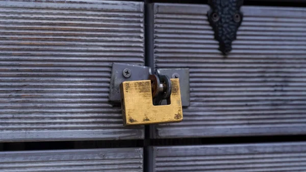 A close-up of a gold-colored metal padlock closes a wooden door. Locked door. wooden door with padlock.