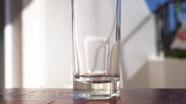 Mutfak arka planındaki sürahide bardağa su dökmek. Parlak güneşli bir balkonda cam bardağa su döker..