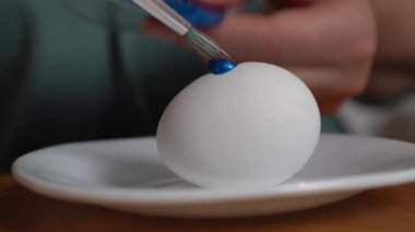 Fırçalı genç bir kız Paskalya bayramı onuruna beyaz bir tabağa beyaz bir tavuk yumurtası çizer. Kapat.