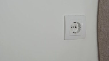 Bir adamın eli, beyaz bir duvara karşı beyaz bir kolyeye güç vermek için siyah bir tel yerleştirir..