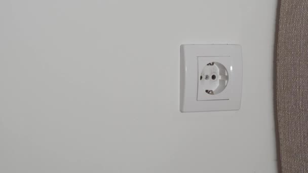 一个男人的手的特写插入一个白色电源适配器 将手机充电到白墙的插座上 — 图库视频影像