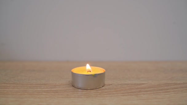 白い壁に向かってテーブルの上に黄色の香りのろうそくの炎を吹く男のクローズアップ — ストック動画