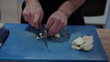 Mavi yaban domuzları üzerinde sarımsak doğrayan tanınmamış erkek ellerine yakın çekim. Aşçı elleri sarımsağı keskin bıçakla kesiyor..
