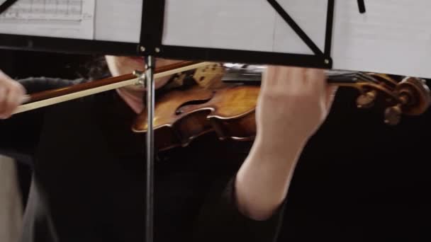 女小提琴家的电影特写是在古典戏剧舞台上的音乐会上与背景上的交响乐团一起演奏小提琴 — 图库视频影像
