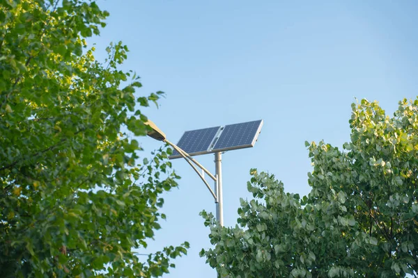 stock image a pole with a street lamp powered by solar panels in the city between trees. High Technologies of Power Engineering