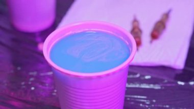 Dövmeci kız, pembe boyayı iğnelerden temizlemek için dövme makinesini mavi suya batırıyor.