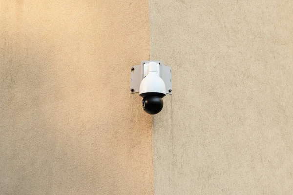 A CCTV camera hangs on the corner of a beige building.