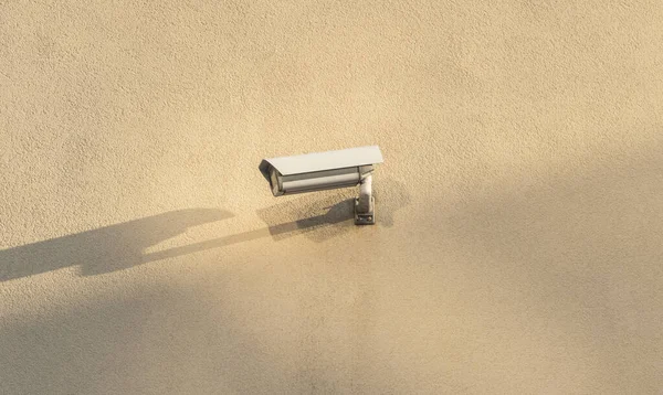 A CCTV camera hangs on the corner of a beige building.