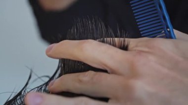 Berber dükkanında saç kesiminin yakın çekimi. Erkek saçını makasla kesen bir adamın yakın çekimi. Kuaför makası ve tarama yardımıyla saç kısaltma.