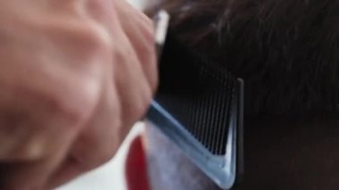 Berber dükkanında saç tıraşı olmuş bir adam. Saç kesimi için erkek saçlarını makasıyla kesen bir adamın yakın çekimi. Saç kesme makası yardımıyla saç kısaltma ve tarama..