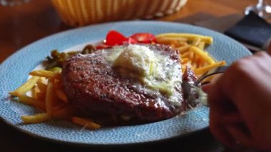 Tabakta bir et parçası kesen bir kızın yakın çekimi. Sokak yemeği. Büyük bir et yemeği ve patates kızartması..